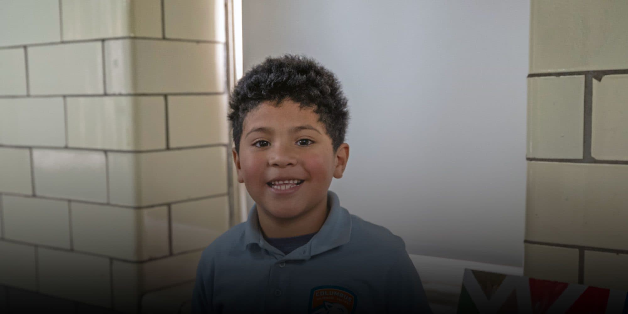 Smiling student in a Columbus Bilingual Central polo in a school hallway.