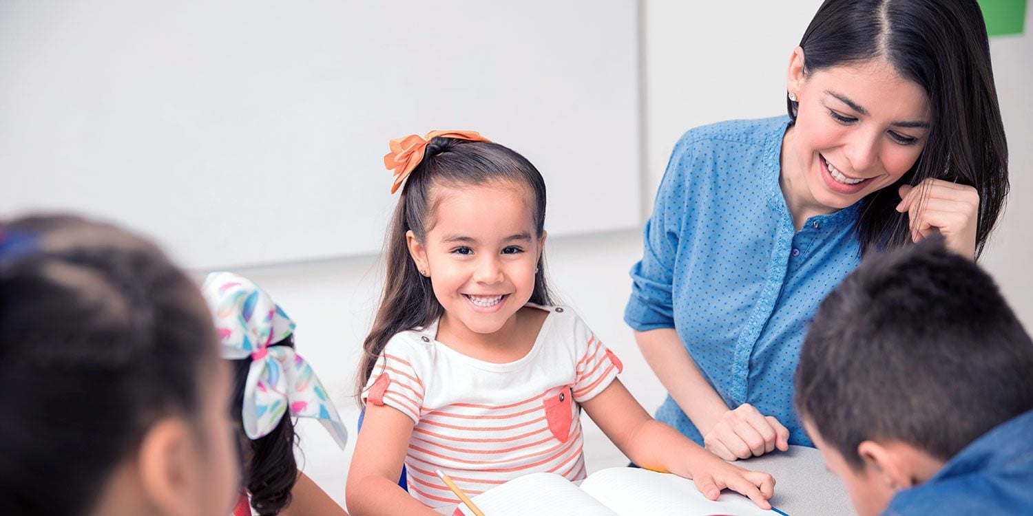Adult and children smiling and interacting in a classroom setting.