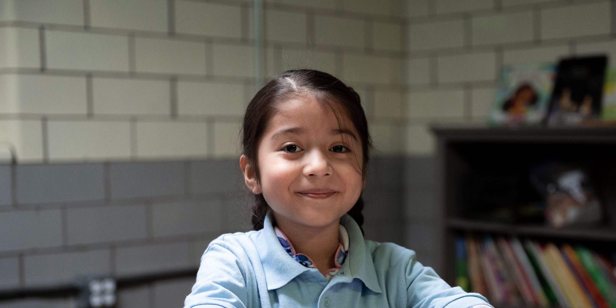 Smiling student in a light blue polo in a classroom.