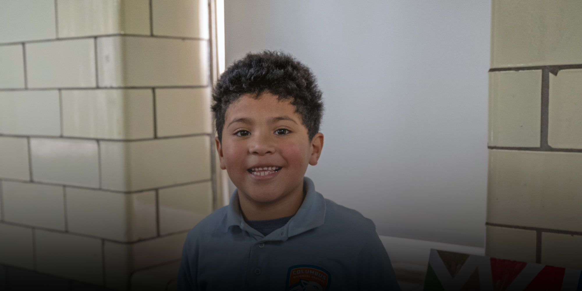 Smiling student in a Columbus Bilingual Central polo in a school hallway.